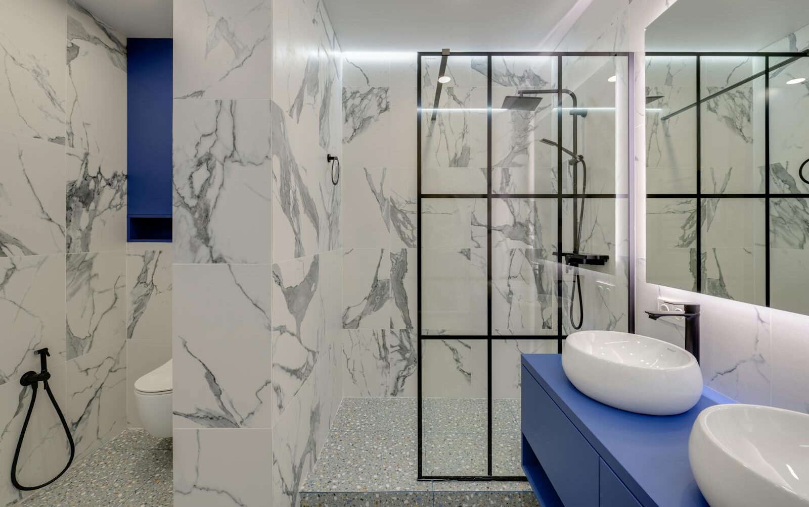 Elegant bathroom featuring marble walls, double sinks, and a glass-enclosed shower.